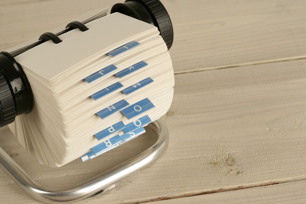 A close-up of a traditional Rolodex with alphabet tabs on a wooden desk.